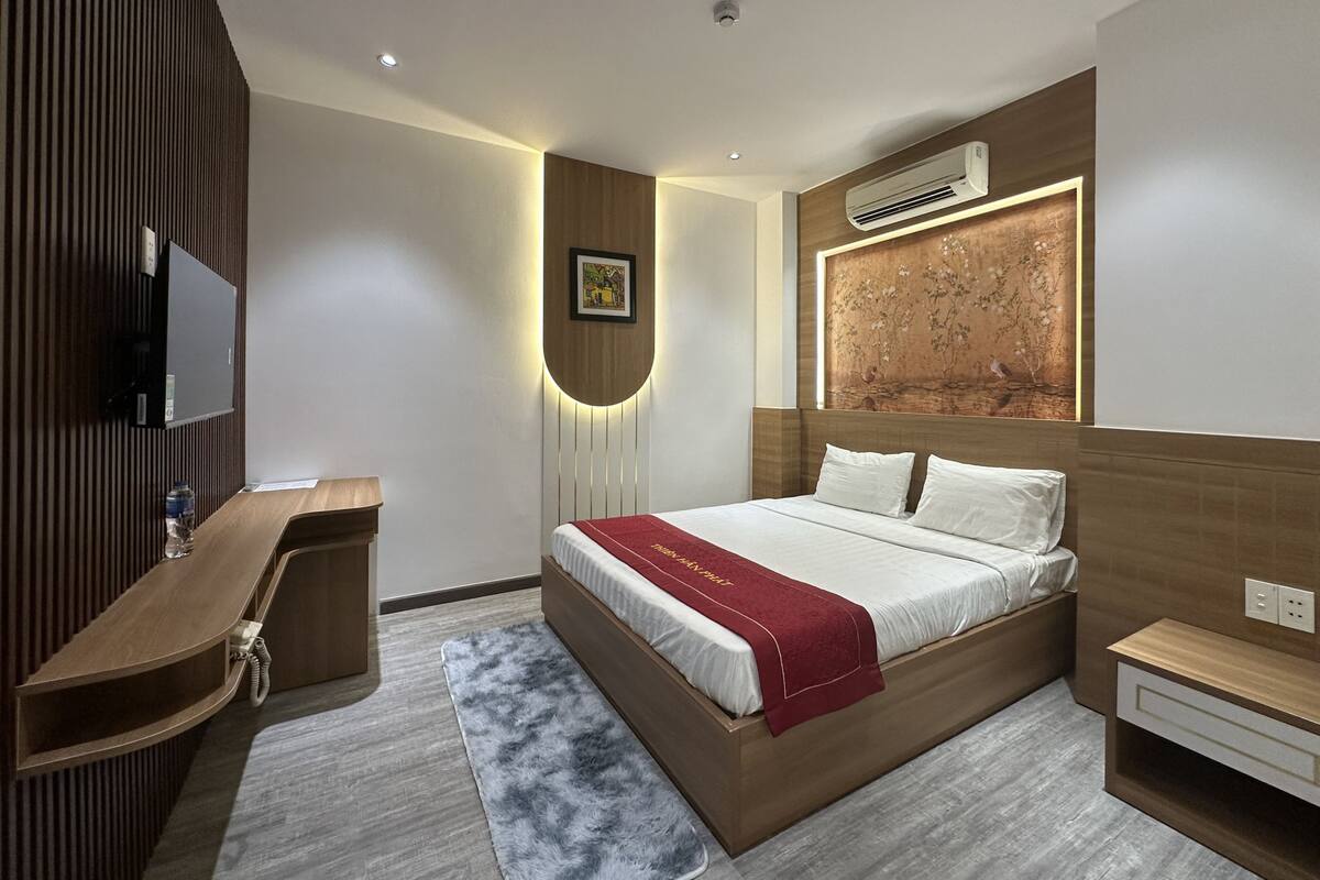 A modern hotel room with a large bed, a desk, a television, and an air conditioning unit.
