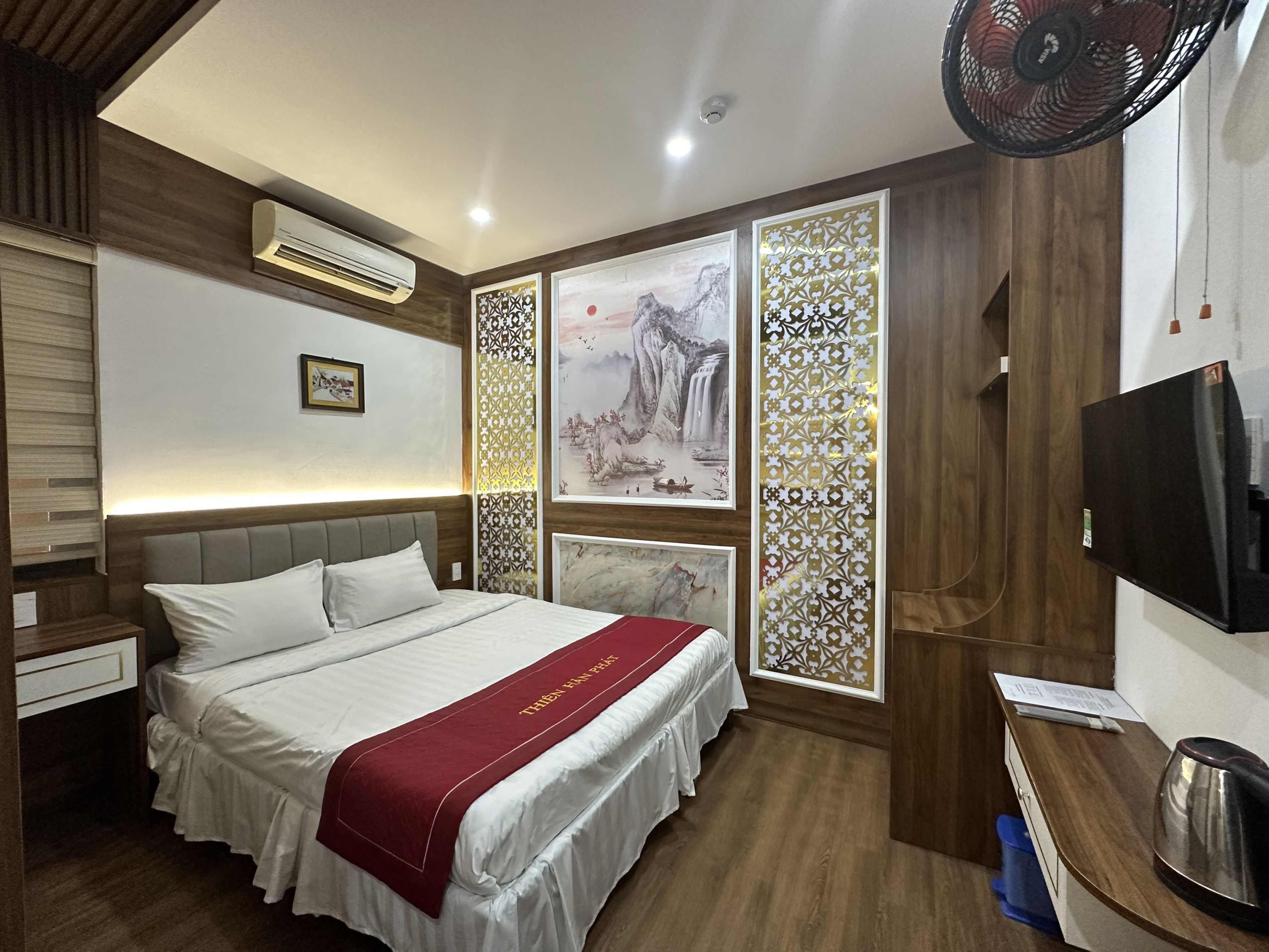 A hotel room with a bed, a desk, a TV, and decorative panels.