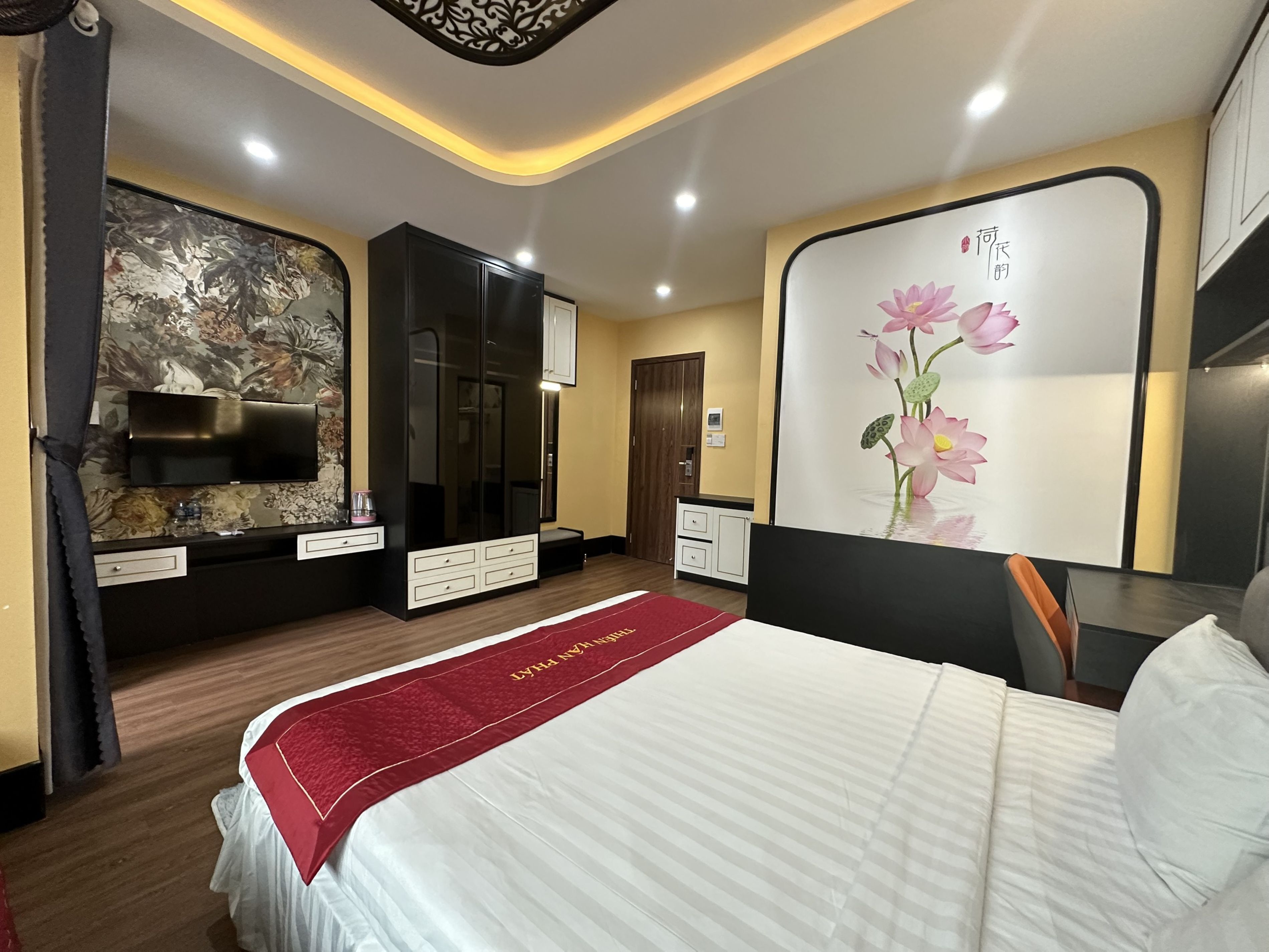 Quarto de hotel com cama, guarda-roupa, televisão e decoração floral na parede.