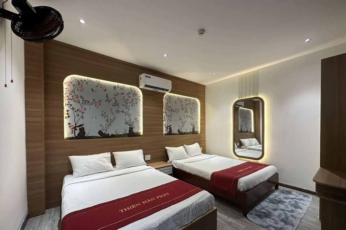 A modern hotel room with two beds, a large mirror, and a decorative wall with floral patterns.