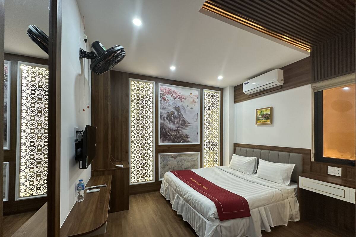 A modern hotel room with a large bed, a desk, and a decorative screen.