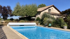 A rectangular swimming pool with a tiled deck, surrounded by a wooden fence and greenery.