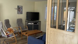 Una sala de estar con piso de madera, un sofá azul, dos sillones escoceses, un televisor y un mueble.