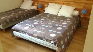 Una habitación con dos camas, cada una con colchón acolchado y colcha de lunares. Hay dos lámparas de noche y un cabecero de madera.