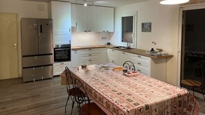 Una cocina moderna con armarios blancos, un refrigerador de acero inoxidable, un horno y una mesa de comedor con sillas.