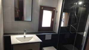 Un baño moderno con lavamanos blanco, espejo, inodoro y cabina de ducha con mampara de vidrio.