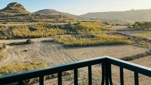 A view from a balcony with a metal railing, overlooking a dry, hilly landscape with sparse vegetation and a clear blue sky. - Del Mar Apartment! (Iż-Żebbuġ)
