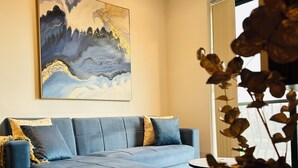 A modern living room with a blue sofa, a small round table, and a large abstract painting on the wall. - Del Mar Apartment! (Iż-Żebbuġ)