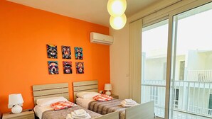 A modern bedroom with two beds, an orange wall, and artwork. - Del Mar Apartment! (Iż-Żebbuġ)