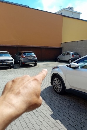 A parking area with several cars, a hand pointing, and a building with a brown and yellow facade. - BnButler - Black Mountain, 62 (Milano)