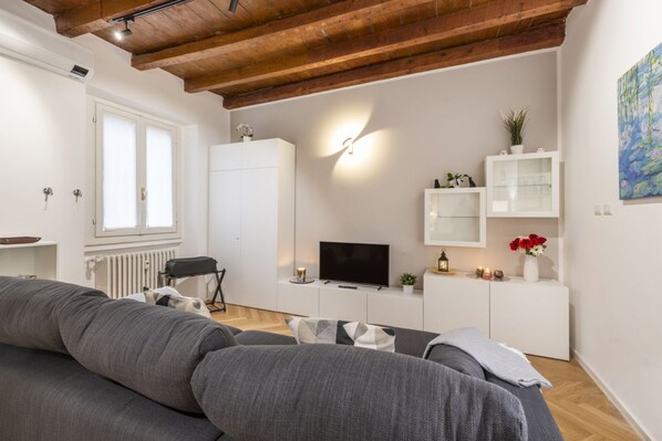 A modern living room with a sofa, TV, white cabinets, and a wooden ceiling.