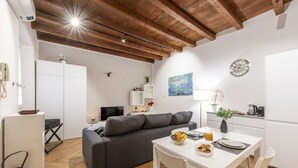A modern living space with a grey sofa, white dining table, and wooden ceiling beams. - BnButler - Black Mountain, 62 (Milano)