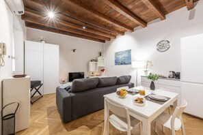 Un espace de vie moderne avec un canapé gris, une table à manger blanche et des poutres en bois au plafond.