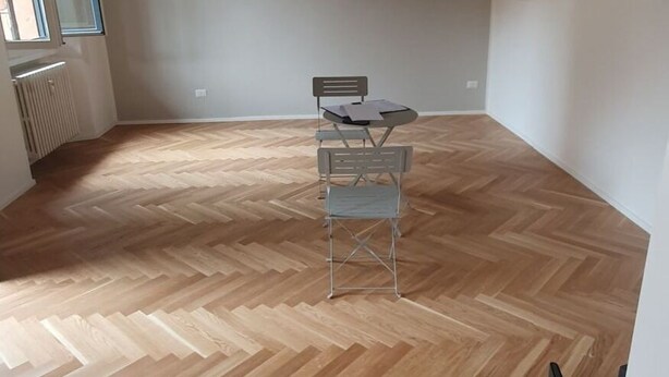 A room with a herringbone wooden floor, a table with chairs, a radiator, and a window. - BnButler - Black Mountain, 62 (Milano)