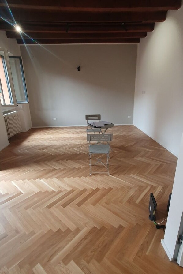 Une pièce avec un parquet en point de Hongrie, une table avec des chaises, un radiateur et une fenêtre.