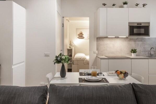 A modern kitchen with white cabinets, a built-in oven, and a dining area with a table set for two. - BnButler - Black Mountain, 62 (Milano)