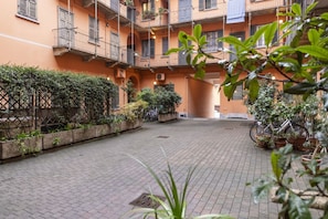 Un cortile con pavimento in piastrelle, piante in vaso e un edificio con balconi.