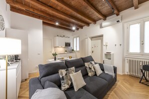 A modern living room with a sofa, a dining area, and a kitchen in the background.