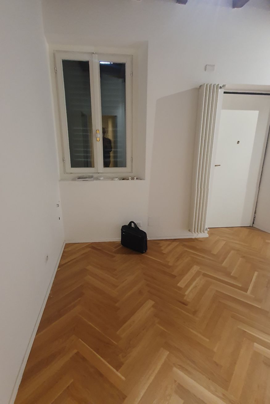 Una habitación con suelo de madera en espiga, una ventana con persianas, un radiador y una puerta.