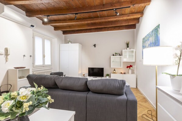 A modern living room with a grey sofa, a flat-screen TV, a white cabinet, and a wooden ceiling.