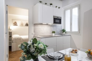 Une cuisine de taille réduite avec des meubles blancs, un four encastré et une fenêtre.