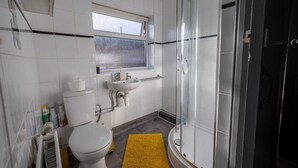 Une salle de bain équipée de toilettes, d’un lavabo, d’une fenêtre et d’une douche à parois de verre.