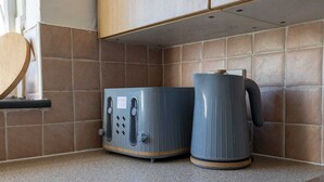 Une petite cuisine équipée d’un four à micro-ondes, d’une machine à café et d’une étagère en bois.