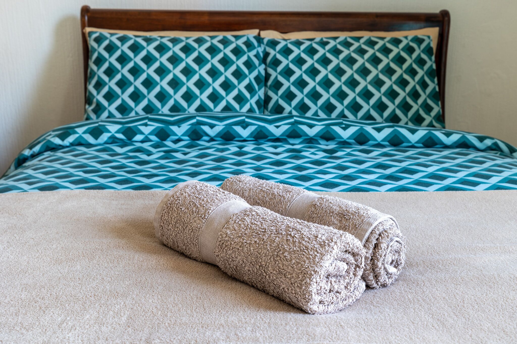 Un lit bien fait, recouvert d’une courtepointe bleue et blanche à motifs, avec deux serviettes enroulées et une tête de lit en bois.
