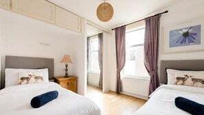 A hotel room with two beds, a nightstand with a lamp, a window with curtains, and a framed picture on the wall. - Stunning 2-bed Apartment in Dartford (Dartford)