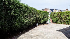 Ein gepflasterter Weg, gesäumt von dichten, grünen Hecken, führt zu einem Gebäude mit Solaranlage auf dem Dach.