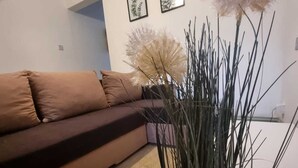 A living room with a brown sofa, a wooden floor, and a potted plant with tall, thin leaves. - Elegant 4-bed House in Dartford (Dartford)