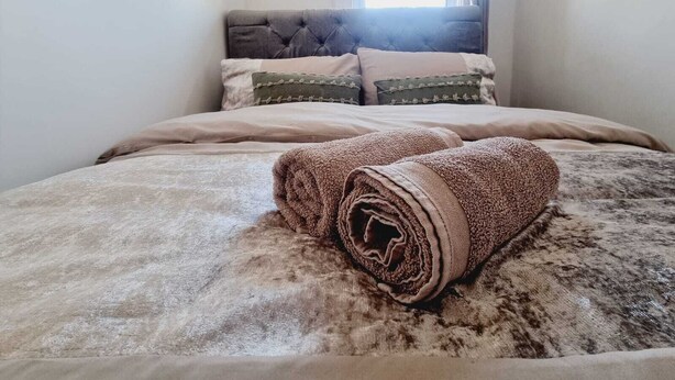 A neatly made bed with a rolled-up blanket in a room with a window and a headboard. - Elegant 4-bed House in Dartford (Dartford)