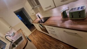 A kitchen with white cabinets, a wooden countertop, a built-in oven, and a green toaster. - Elegant 4-bed House in Dartford (Dartford)