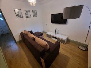 A modern living room with a dark brown sofa, a white TV stand, and a floor lamp. - Elegant 4-bed House in Dartford (Dartford)