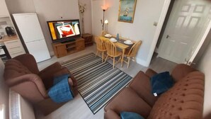 A living room with two brown sofas, a television, a dining table with chairs, and a kitchen area with a refrigerator. - Gorgeous 4-bedroom House in Orpington (Orpington)