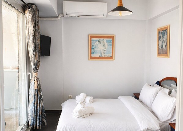 A hotel room with a bed, a television, a painting, and an air conditioning unit.