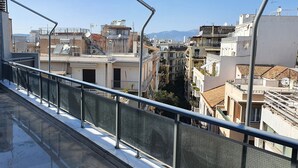 A rooftop terrace with a metal railing, potted plants, and a view of a cityscape with buildings and mountains in the distance.