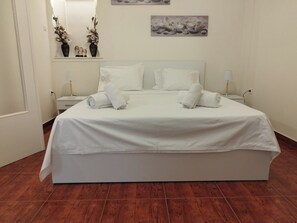 A neatly made bed with white linens and towels, a bedside table with a lamp, and a wall-mounted picture. - Zeus Apartment Athens (Athens)