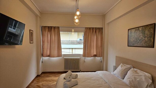 A hotel room with a bed, a TV, a radiator, and a window with curtains. - F23 Athens Apartment (Athens)