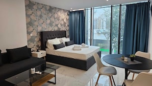 A modern hotel room with a large bed, a sofa, a coffee table, and a dining table.