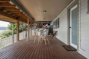 Une terrasse en bois couverte, avec une table et des chaises, un banc et une porte donnant sur une maison.
