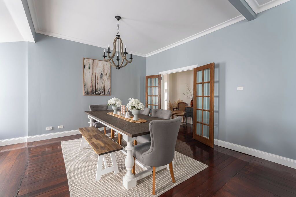 A dining room with a dark wooden table, white chairs, a chandelier, and a painting on the wall.