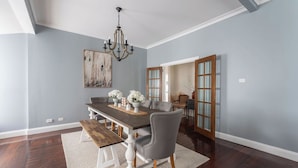 A dining room with a dark wooden table, white chairs, a chandelier, and a painting on the wall. - View Point: Ocean Views & Near CBD (Burnie)