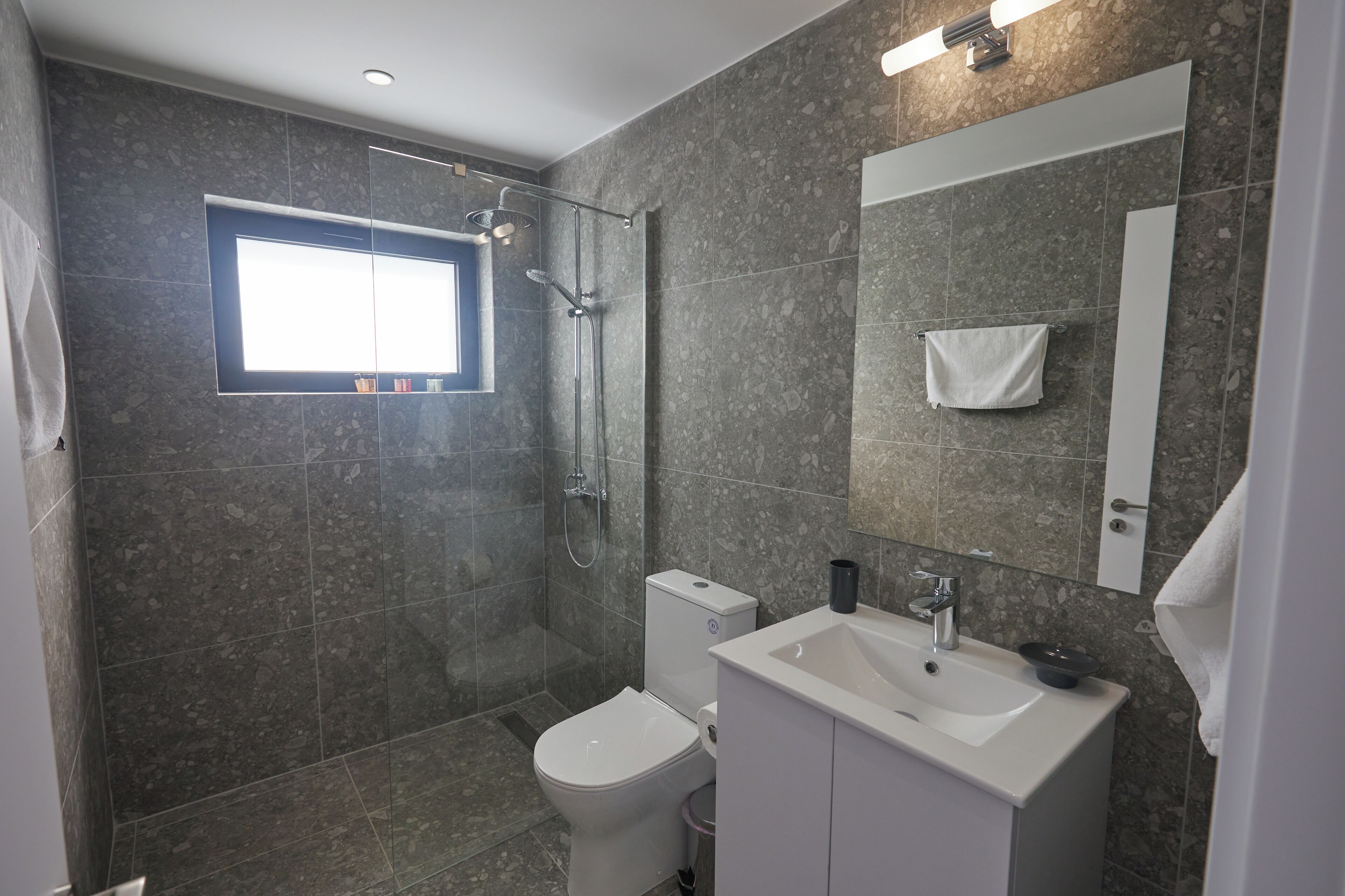 A modern bathroom with a shower, toilet, sink, and a large mirror.