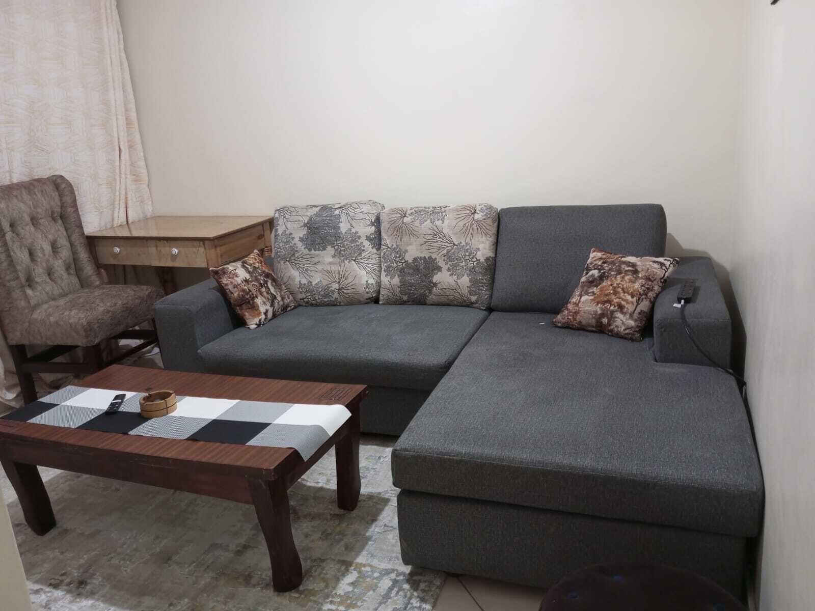 Un salon avec un canapé gris, une chaise en bois, une petite table et des coussins à motifs.
