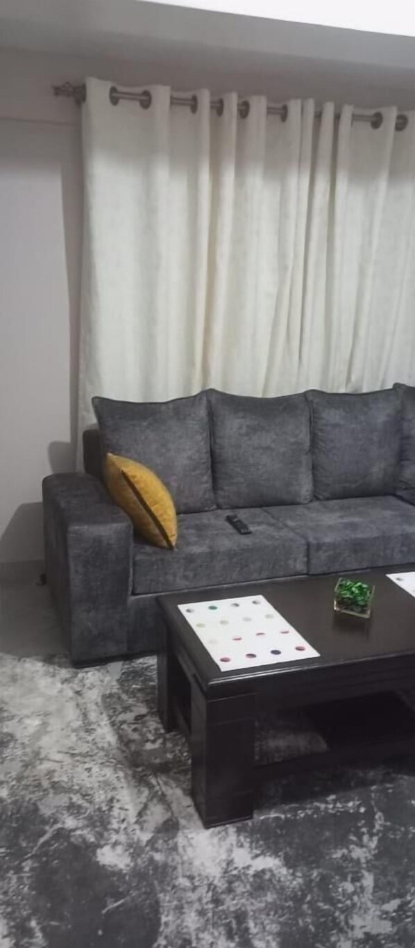 A living room with a grey sofa, a yellow pillow, a remote control, and a coffee table with a card and a small plant.
