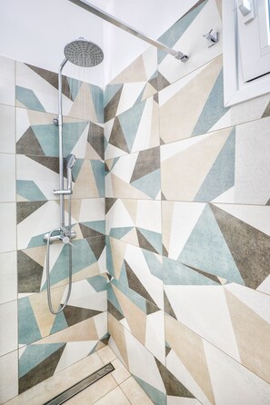 A shower with a handheld showerhead and a wall-mounted faucet. The shower area has a geometric tile pattern on the walls.
