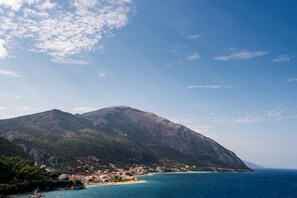 A coastal town with a prominent mountain, clear blue sea, and a small lighthouse.