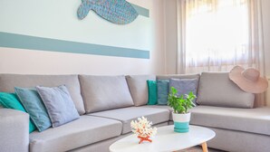 Un salón moderno con un sofá gris, cojines color turquesa, una mesa de centro blanca con una planta y una decoración de peces montada en la pared.
