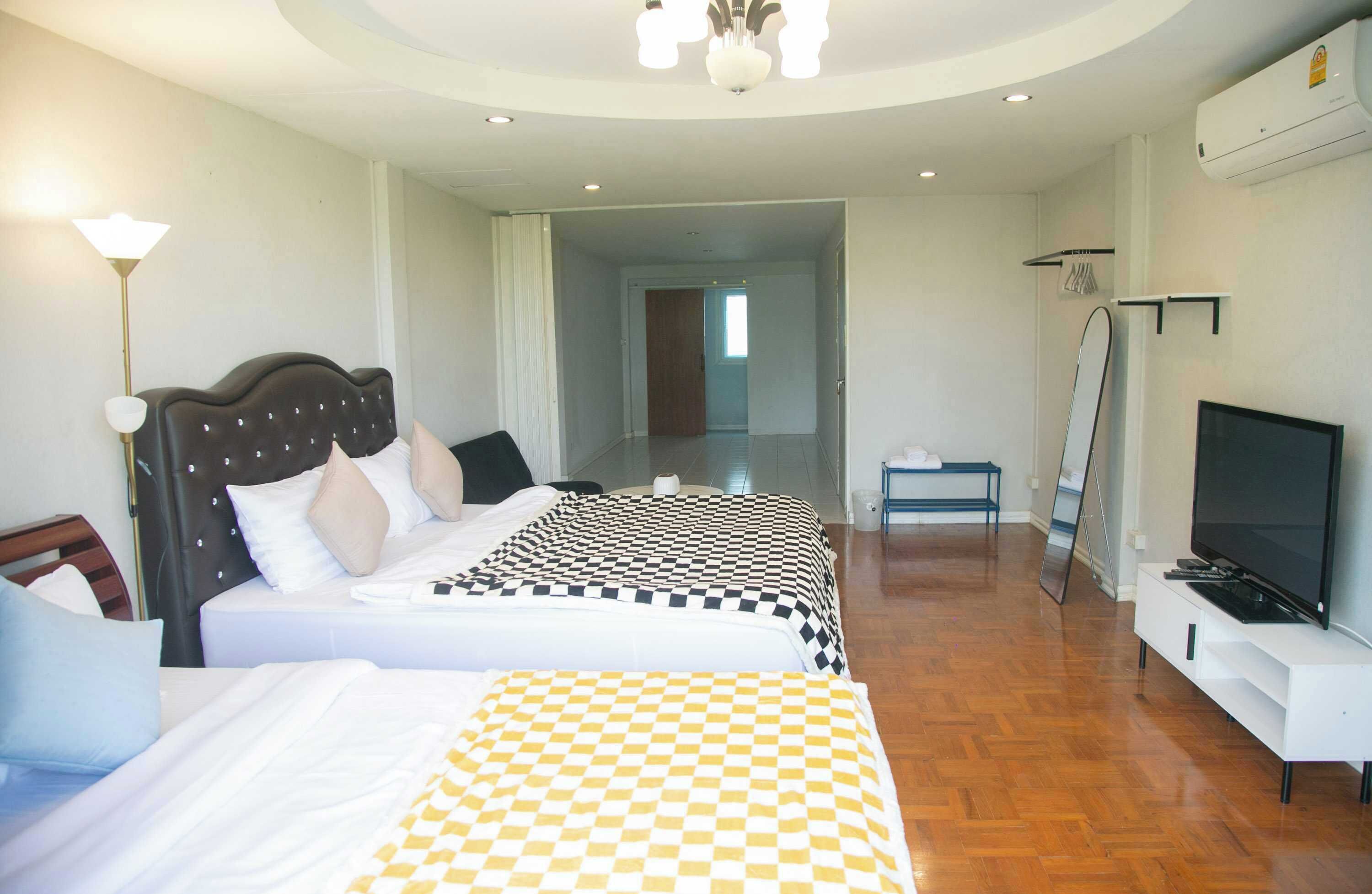 A hotel room with two beds, a TV, a mirror, and a hallway leading to another room.